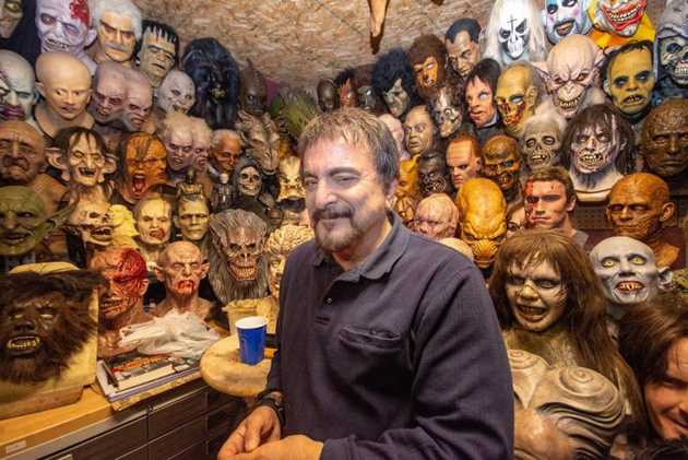 Tom Savini rodeado de máscaras de montros dos filmes de terror.